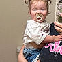 adult_hand, bathroom, casual_clothing, child, cute, denim_shorts, holding, indoor, lace_trim, mirror_selfie, pacifier, person, phone_case, pigtails, pink_text, portrait, smiling, toddler, toilet, white_shirt