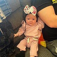 Aria joined the competition — help win amazing prizes! baby, infant, child, pajamas, bow, headwear, couch, sofa, adult_arm, blanket, home, cozy, textile, person, sitting, black_socks, pink_clothing, cute, indoor, relaxing