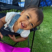 Zia is registered to the contest to win money with this photo: child, toddler, smiling, happy, face, hair, clothing, denim_overalls, chair, outdoor, grass, bag, pink, people, background, daylight, playful, portrait, person, fun
