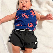 Ayden joined the competition — help win amazing prizes! baby, infant, child, blue_tank_top, crab_pattern, black_shorts, blanket, soft_texture, lying_down, indoor, cute, expression, skin, arms, legs, face, hair, clothing, person, young