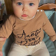 Théa participe au concours pour gagner de l'argent avec cette photo : baby, child, blue_eyes, headband, brown_shirt, text_on_clothing, sitting, mickey_mouse, cushion, indoor, wooden_chair, cute, portrait, infant, clothing, person, young_child, pink_socks, cozy, expression