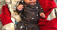 Maverick is registered to the contest to win money with this photo: baby, infant, child, portrait, sitting, blanket, red_blanket, pajamas, sleepwear, dark_clothing, bare_feet, indoors, cozy, carpet, rug, chair, bedding, wide_eyes, looking_at_camera, cute