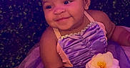 Naomi is registered to the contest to win money with this photo: baby, child, portrait, smiling, dress, purple, pink, tutu, flower, headband, bow, outdoor, foliage, garden, sitting, infant, fashion, costume, colorful_lighting, happy