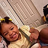 Naomi is registered to the contest to win money with this photo: child, toddler, girl, smiling, happy, portrait, indoor, bedroom, hairbrush, yellow_dress, hair_bows, curly_hair, sitting, close_up, face, teeth, arm, hand, door, home