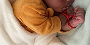 Kaylon a rejoint le concours — aidez-le/la à gagner de superbes lots ! baby, sleeping, blanket, cozy, infant, child, soft, yellow_clothing, red_bracelet, peaceful, cute, indoors, resting, portrait, newborn, curly_hair, toddler, hands, face, bed