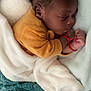 baby, sleeping, blanket, cozy, infant, child, soft, yellow_clothing, red_bracelet, peaceful, cute, indoors, resting, portrait, newborn, curly_hair, toddler, hands, face, bed