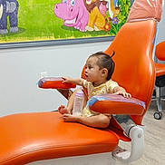 Zoey is registered to the contest to win money with this photo: antelope, baby_bottle, bright_colors, cartoon_mural, child, curious, dental_chair, floor, gorilla, hippopotamus, hospital_setting, indoor, lion, medical_office, orange_chair, plastic_cover, sitting, toddler, wall, young_child