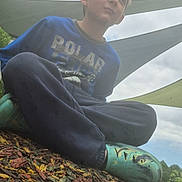 Colten joined the competition — help win amazing prizes! child, boy, sitting, cross_legged, blue_shirt, green_shoes, playground, wood_chips, outdoor, shade_cloth, cloudy_sky, casual_clothing, young, daylight, nature, relaxing, leisure, expression, park, footwear