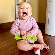 Evelina joined the competition — help win amazing prizes! baby, child, laughing, pink_clothing, sitting, wooden_floor, toy, green_toy, red_ball, white_ball, happy, indoor, person, infant, cute, smiling, playful, floor, head, hand