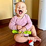 baby, child, laughing, pink_clothing, sitting, wooden_floor, toy, green_toy, red_ball, white_ball, happy, indoor, person, infant, cute, smiling, playful, floor, head, hand