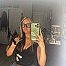 woman, cat, mirror, selfie, glasses, black_cat, jewelry, room, door, coat, smartphone, casual_clothing, jeans, long_hair, indoor, personal_items, reflection, hand, fingernails, accessories