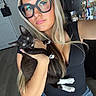 woman, glasses, cat, kitten, black_cat, white_paws, selfie, blonde_hair, jewelry, bracelets, indoor, door, hand, face, black_shirt, long_hair, home, floor, casual, expression