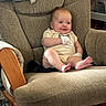 Aurora is registered to the contest to win money with this photo: baby, infant, smile, face, armchair, cushion, clothing, mittens, furniture, wood, happy, sitting, indoors, child, cute, cheeks, legs, feet, comfortable, portrait