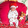 baby, blanket, celebration, child, christmas, cute, festive, holiday, indoors, infant, lying_down, pajamas, plush_toy, red_cushion, reindeer, santa_hat, sleepwear, smiling, soft_toy, toy_car