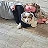 person, dog, puppy, australian_shepherd, floor, wooden_floor, hugging, lying_down, sleeping, cozy, pet, cute, fur, black_sleeve, gray_sweater, indoor, home, relaxation, animal, companion
