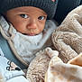 baby, child, toddler, beanie, hat, blanket, car_seat, bib, closeup, portrait, eyes, gaze, hand, cozy, soft_texture, fleece, warmth, mischievous_expression, infant_clothing, car_trip