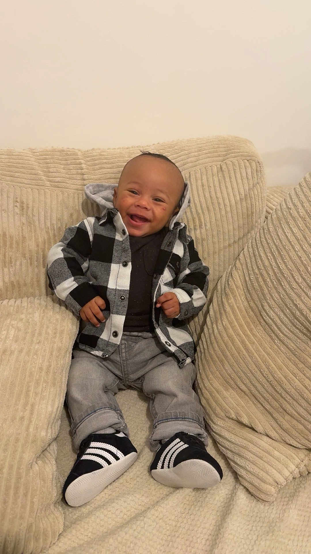 Ayden a rejoint le concours — aidez-le/la à gagner de superbes lots ! baby, infant, smiling, plaid_shirt, hoodie, jeans, sneakers, socks, couch, cushion, pillow, blanket, portrait, face, hands, seated, home_interior, happy, shoe_stripes, cozy