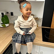 Rym participe au concours pour gagner de l'argent avec cette photo : bandage, blister_pack, boots, child, countertop, curly_hair, happy, indoor, kitchen, modern_kitchen, person, plaid_skirt, plant, portrait, sitting, smiling, sweater, toddler, white_cabinet, wooden_countertop