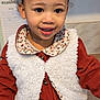 toddler, child, smiling, curly_hair, bun, vest, dress, floral_collar, buttoned_clothing, indoor, planner, face, happy, person, portrait, cute, young_child, warm_clothing, skin, eyes