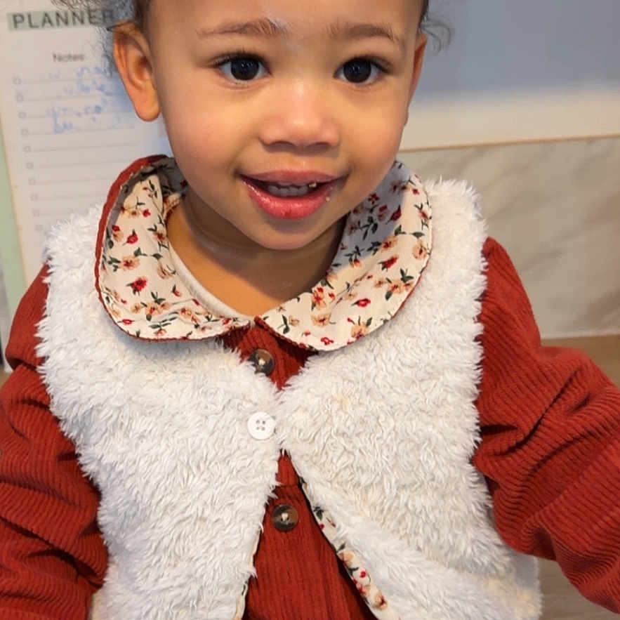 Rym a rejoint le concours — aidez-le/la à gagner de superbes lots ! bun, buttoned_clothing, child, curly_hair, cute, dress, eyes, face, floral_collar, happy, indoor, person, planner, portrait, skin, smiling, toddler, vest, warm_clothing, young_child