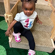 La'Rae is registered to the contest to win money with this photo: toddler, child, girl, smiling, hair_bows, white_shirt, number_one, leggings, pink_sneakers, carpeted_stairs, wooden_play_structure, indoor, play_area, green_carpet, cute, happy, sitting, person, young_child, playtime