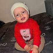 Sami is registered to the contest to win money with this photo: baby, blanket, child, clothing, cozy, cute, face, footwear, happy, hat, holiday, indoor, knit_hat, luxury_brand, portrait, red_sweater, sitting, smiling, toddler, young_child