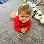 Sami is registered to the contest to win money with this photo: toddler, child, carpet, red_shirt, toy, plush_animal, indoor, smiling, cute, playroom, diaper, clothing, floor, person, baby_toy, stuffed_animal, hands, eyes, hair, expression