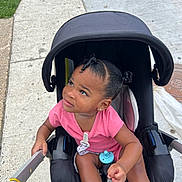 Ailany is registered to the contest to win money with this photo: toddler, child, stroller, pink_shirt, pacifier, sidewalk, grass, outdoor, curious, sitting, black_stroller, hair_twists, footwear, daylight, person, handlebar, concrete, urban, young_child, casual
