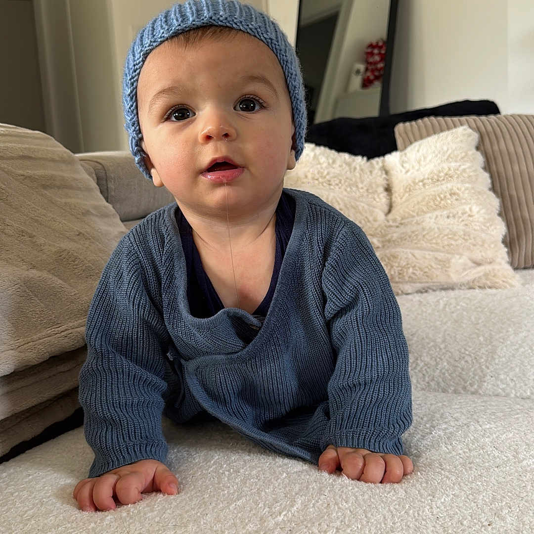 éli a rejoint le concours — aidez-le/la à gagner de superbes lots ! baby, blue_hat, blue_sweater, child, cozy, crawling, curious_expression, cushions, drool, face, furniture, hands, headwear, home, indoor, knitwear, mirror, person, portrait, soft_texture