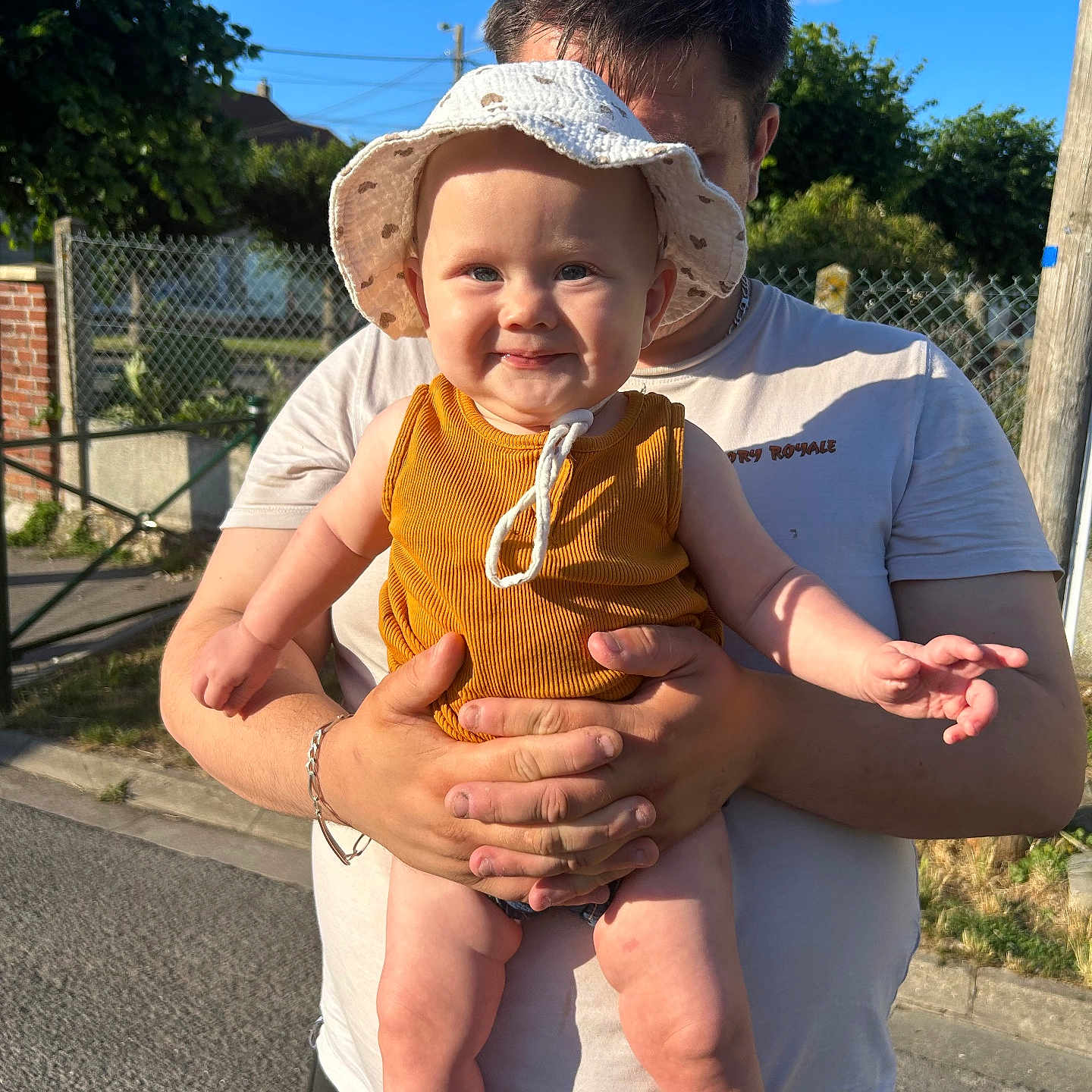Romy participe au concours pour gagner de l'argent avec cette photo : adult, baby, blue_sky, casual, child, clothing, daylight, family, fence, happy, hat, holding, nature, outdoor, person, portrait, smile, street, sun_hat, tree
