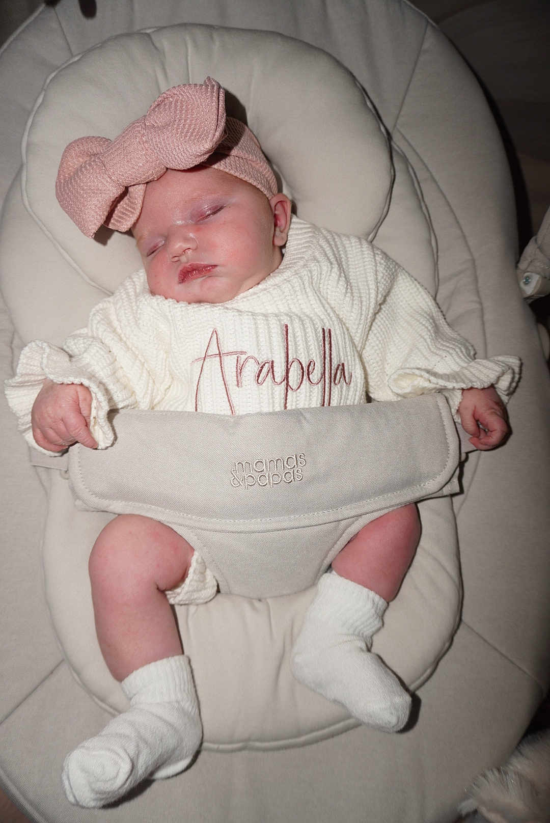 Arabella is registered to the contest to win money with this photo: baby, sleeping, headband, bow, white_sweater, embroidery, name, arabella, cushioned_seat, infant, sock, soft_fabric, hands, legs, pink, comfortable, child, resting, cute, indoors