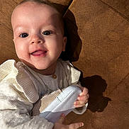 Héléna participe au concours pour gagner de l'argent avec cette photo : baby, infant, smile, face, hand, shoe, white_clothing, couch, brown_fabric, happy, cute, portrait, child, indoors, cozy, texture, soft, young, playful, closeup