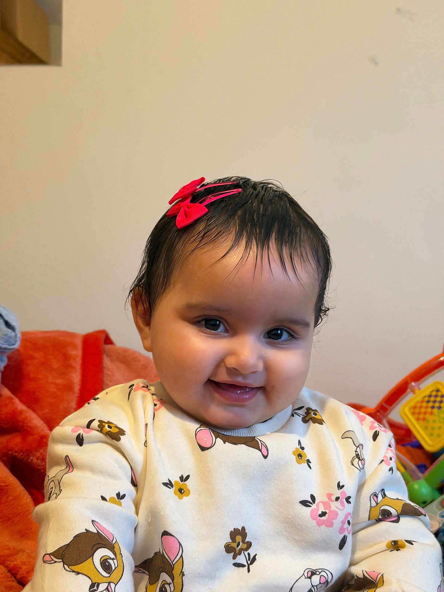 Jind is registered to the contest to win money with this photo: baby, child, smiling, sweater, red_bow, cartoon_print, indoor, toy, blanket, cute, portrait, happy, face, young_child, clothing, person, closeup, infant, warm, playful