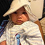 baby, child, hat, onesie, striped_clothing, embroidered_character, indoor, person, portrait, cute, wide_eyes, hand, adult_arm, fabric, soft_lighting, close_up, face, expression, cozy, infant