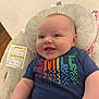 Flynn is registered to the contest to win money with this photo: baby, smiling, infant, tshirt, colorful_text, cushion, seat, indoor, happy, child, skin, cheeks, eyes, clothing, person, cute, portrait, babywear, relaxing, comfort