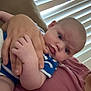 Flynn is registered to the contest to win money with this photo: baby, infant, person, hand, couch, window_blinds, blue_clothing, adult_hand, indoor, closeup, face, skin, expression, seated, holding, comfort, furniture, casual, portrait, home