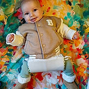 Maddie participe au concours pour gagner de l'argent avec cette photo : baby, infant, smile, tongue_out, colorful_background, floral_pattern, blanket, warm_clothing, jacket, boots, leggings, cute, portrait, lying_down, happy, child, cozy, indoor, playful, person