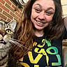 woman, cat, tabby_cat, smile, long_hair, indoor, brick_wall, tshirt, curious, happy, pet, feline, closeup, face, eyes, whiskers, casual, selfie, person, expression