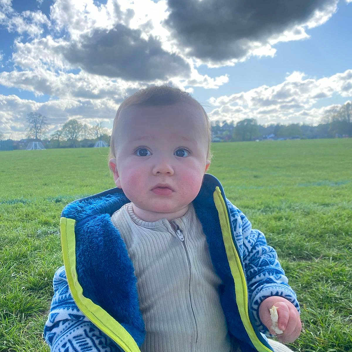 Louie-Tommy joined the competition — help win amazing prizes! baby, blue, child, clouds, curious, daylight, expression, face, field, grass, green, jacket, nature, outdoor, person, sippy_cup, sitting, sky, snack, warm_clothing