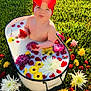 baby, red_bow, headband, tub, milk_bath, strawberries, flowers, grass, outdoor, sunlight, pout, cute, colorful, nature, playful, summer, greenery, yellow_flowers, white_flowers, purple_flowers