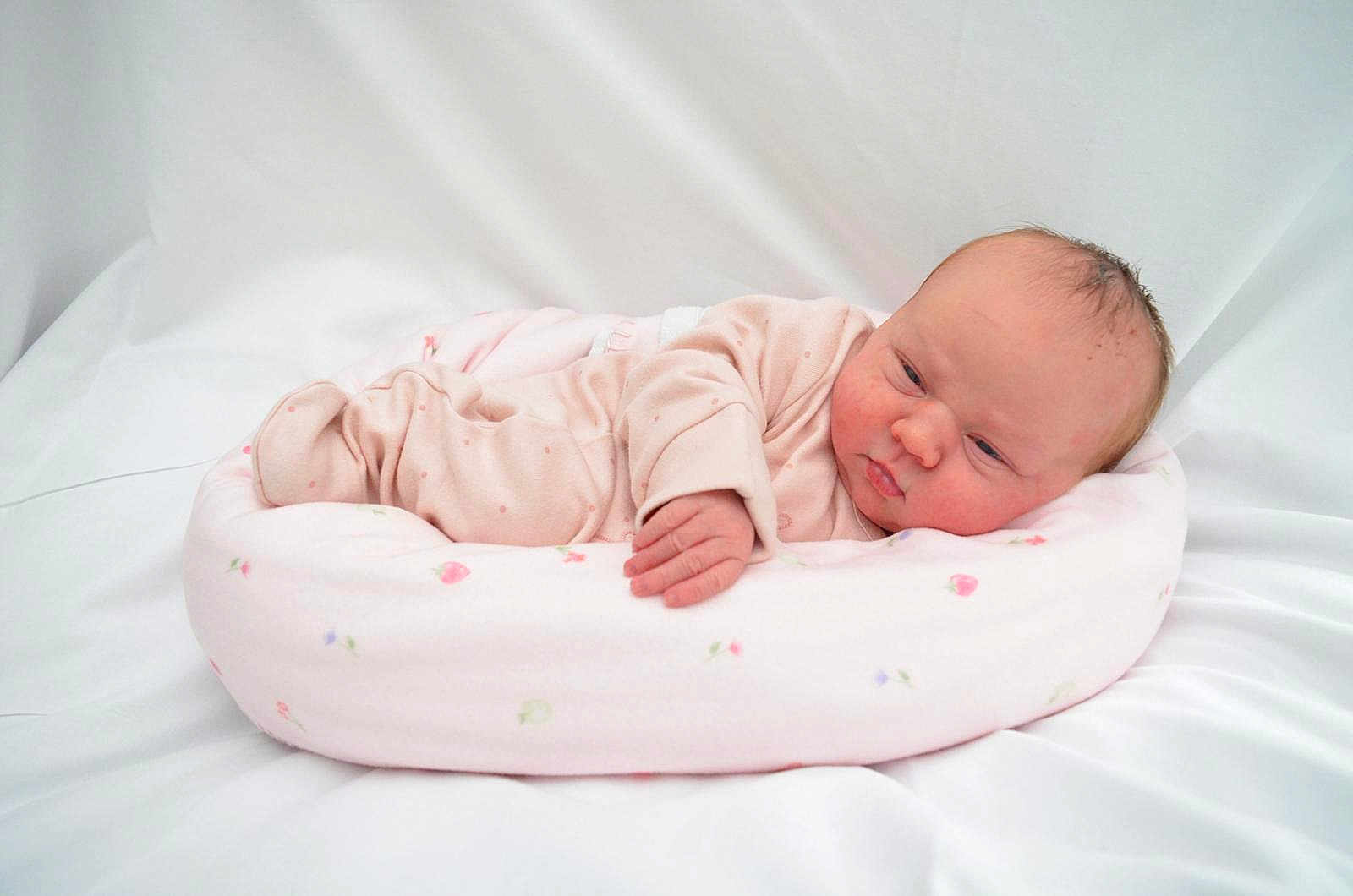 Emie-Grace is registered to the contest to win money with this photo: newborn, baby, infant, pink_onesie, cushion, floral_pattern, soft, sleeping, lying_down, white_background, cute, child, portrait, indoors, cozy, small_hand, head, peaceful, skin, baby_bed