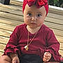 baby, child, red_bow, headband, red_top, ruffled_sleeves, wooden_deck, sitting, barefoot, necklace, food_crumbs, cute, portrait, outdoor, young_child, expression, hands, legs, face, curious