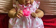 Aniyrah Scott is registered to the contest to win money with this photo: baby, child, infant, dress, headband, bow, pink, heart_pattern, blanket, lying_down, cute, chubby_cheeks, indoors, soft_texture, fabric, person, skin, legs, hands, curious