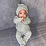 Aniyrah Scott is registered to the contest to win money with this photo: baby, infant, knitted_outfit, hat, thumb_sucking, cute, cozy, grey_couch, seated, child, indoor, fabric, soft_texture, portrait, person, young_child, comfortable, casual, home, small