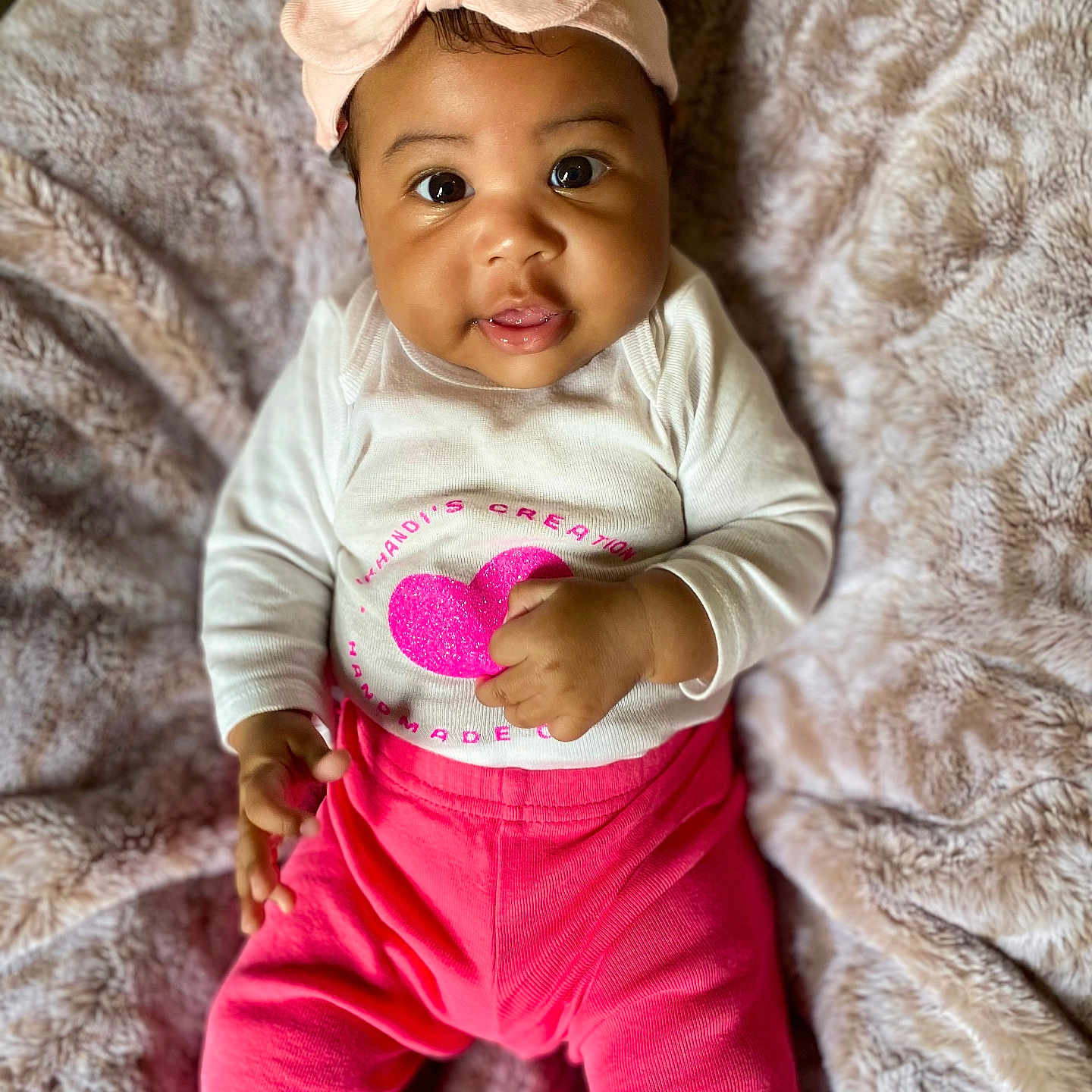 Aniyrah Scott is registered to the contest to win money with this photo: adorable, baby, blanket, child, closeup, cozy, cute, face, happy, headband, indoors, infant, lying_down, pink_bow, pink_pants, portrait, small_hands, smiling, soft_texture, white_shirt