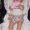 baby, child, infant, stroller, portrait, sitting, lying_down, smiling, curly_hair, pink_mittens, baby_clothes, shorts, frilly_socks, blanket, striped_fabric, floral_blanket, indoor, cozy, face, photography