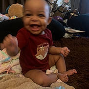 Kailani joined the competition — help win amazing prizes! baby, blanket, blurred, child, couch, curtain, face, foot, hand, happy, home, indoor, infant, pattern, person, red_shirt, sitting, smile, towel, toys