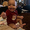 baby, blanket, blurred, child, couch, curtain, face, foot, hand, happy, home, indoor, infant, pattern, person, red_shirt, sitting, smile, towel, toys