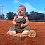 baby, infant, child, overalls, baseball_field, home_plate, outdoor, sky, trees, grass, dirt, sign, milestone, socks, cute, portrait, smiling, fist, daylight, nature
