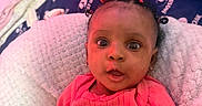 Thalia joined the competition — help win amazing prizes! baby, infant, child, portrait, wide_eyed, red_bow, pink_clothing, coral_outfit, smiling, surprised, sitting, blanket, fluffy_blanket, bed, bedding, pillow, indoor, close_up, face, photography